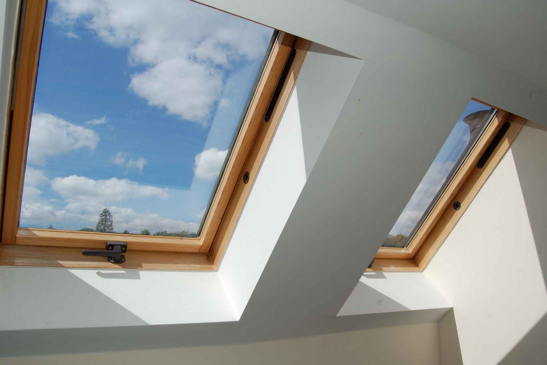 Two roof skylight windows with bright sunlight streaming through the glass into a bright room.